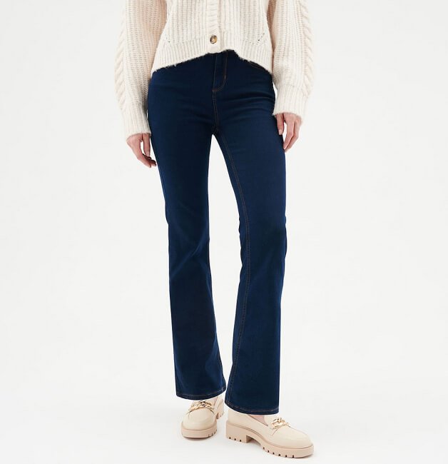 A woman wearing darkwash jeans, a cream knitted cardigan and cream loafers